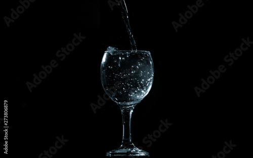 Pour water into glass on black background.
