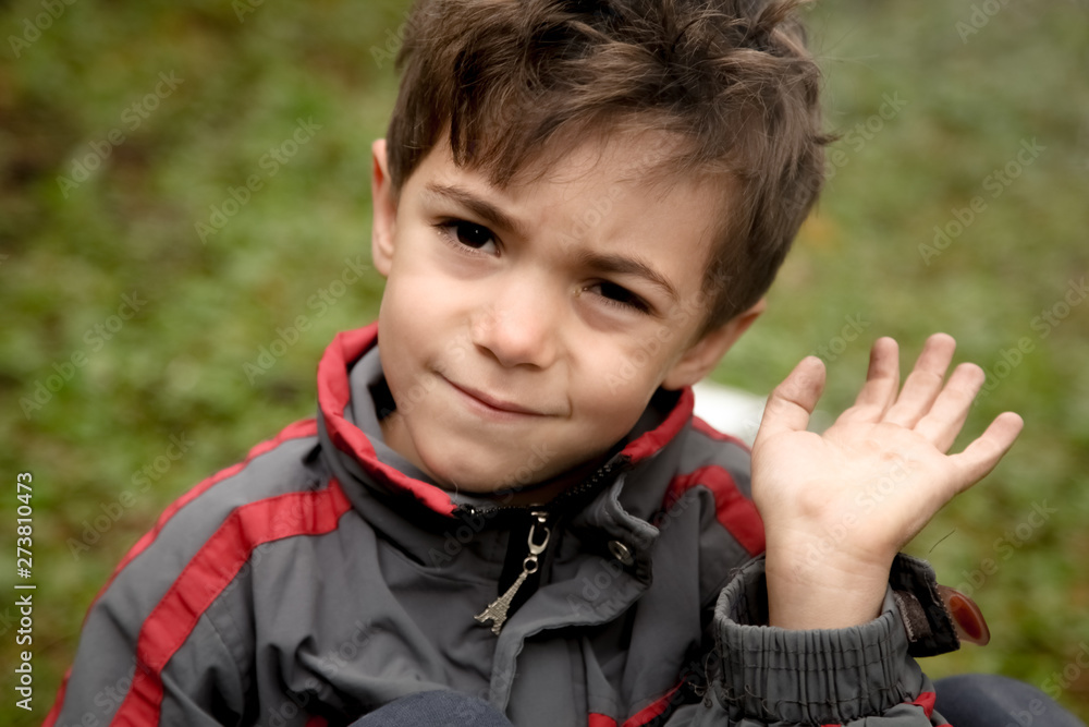 A crying afghan boy waves his hand. On the boy's gray tracksuit with a zipper in the shape of the Eiffel Tower A crying afghan boy waves his hand. On the boy's gray tracksuit with a zipper in the shape of the Eiffel Tower