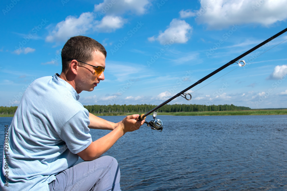 a man in yellow glasses on the pier, throws spinning, fishing, against the blue lake and sky a man in yellow glasses on the pier, throws spinning, fishing, against the blue lake and sky