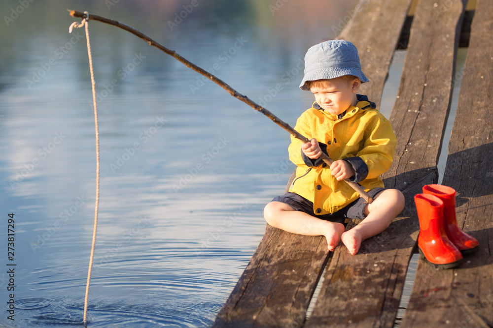 A little boy fishing and wants to catch the biggest fish. Picturesque scene  of cute little boy fishing from wooden dock on magical lake at sunny summer  day, vivid colors Stock Photo