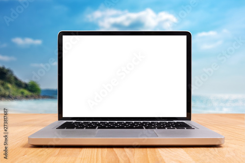 laptop computer with empty blank white screen for copy space on wooden desk with blurry summer sea ocean beach at background © asiandelight