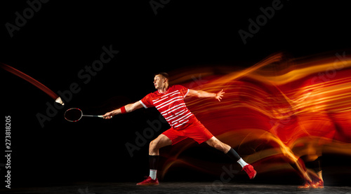 Young man playing badminton isolated on black background in mixed light. Male model with the racket in action, motion in game with the fire shadows. Concept of sport, movement, healthy lifestyle. © master1305
