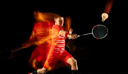 Young man playing badminton isolated on black background in mixed light. Male model with the racket in action, motion in game with the fire shadows. Concept of sport, movement, healthy lifestyle.
