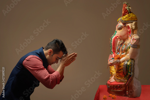 Man praying with hands joined and eyes closed in front of Ganpati Idol.	 photo