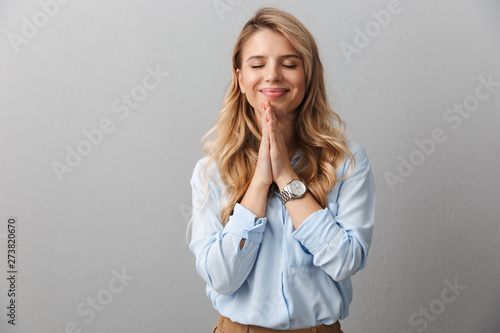 Photo of alluring blond businesswoman with long curly hair smiling and praying with palms together