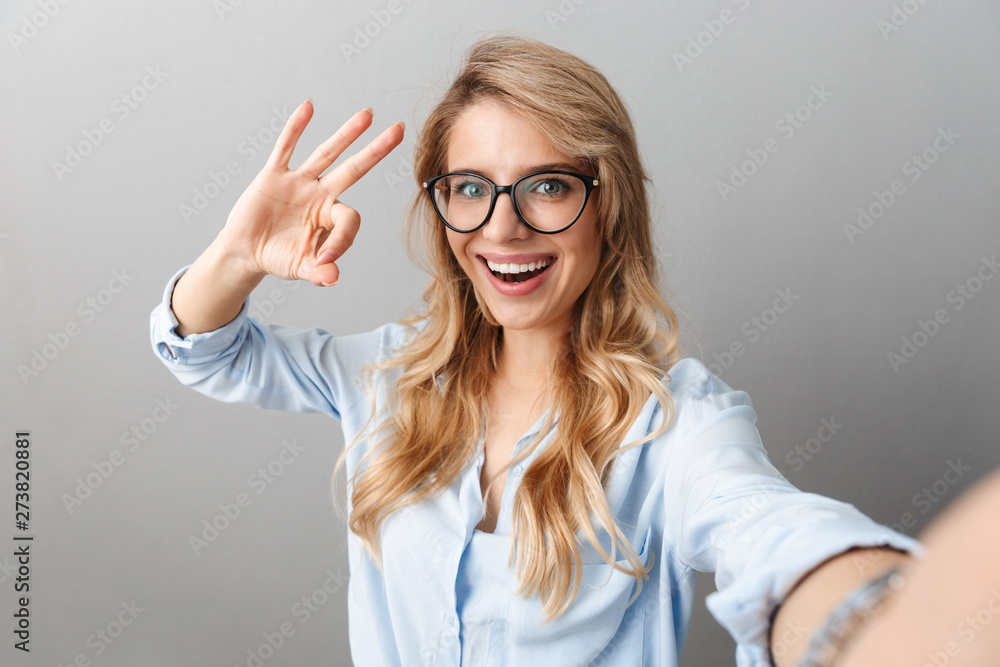 Photo of pretty blond businesswoman wearing eyeglasses smiling and showing ok sign while taking selfie Photo of pretty blond businesswoman wearing eyeglasses smiling and showing ok sign while taking selfie