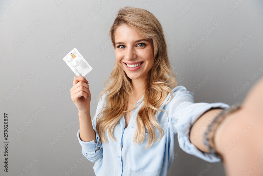Photo of lovely blond businesswoman smiling and holding credit card while taking selfie - obrazy, fototapety, plakaty 