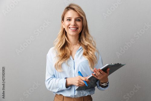 Photo of gorgeous blond secretary woman with long curly hair writing down notes in clipboard while working in office photo