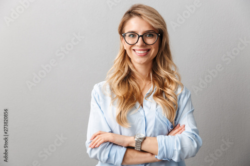 Photo of happy blond businesswoman wearing eyeglasses smiling and standing with hands crossed photo