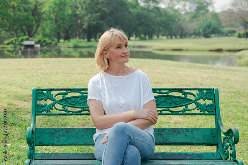 Lonely elderly woman sitting on a bench in a city park background