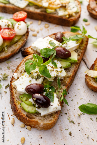 Open sandwich made of slices of sourdough bread with avocado, feta cheese, kalamata olives, olive oil and oregano on a wooden white table, close-up. Vegetarian food