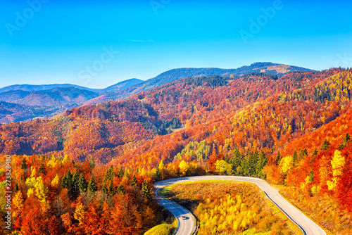 Scenic alpine winding road in autumn mountains with colorful trees and blue s...