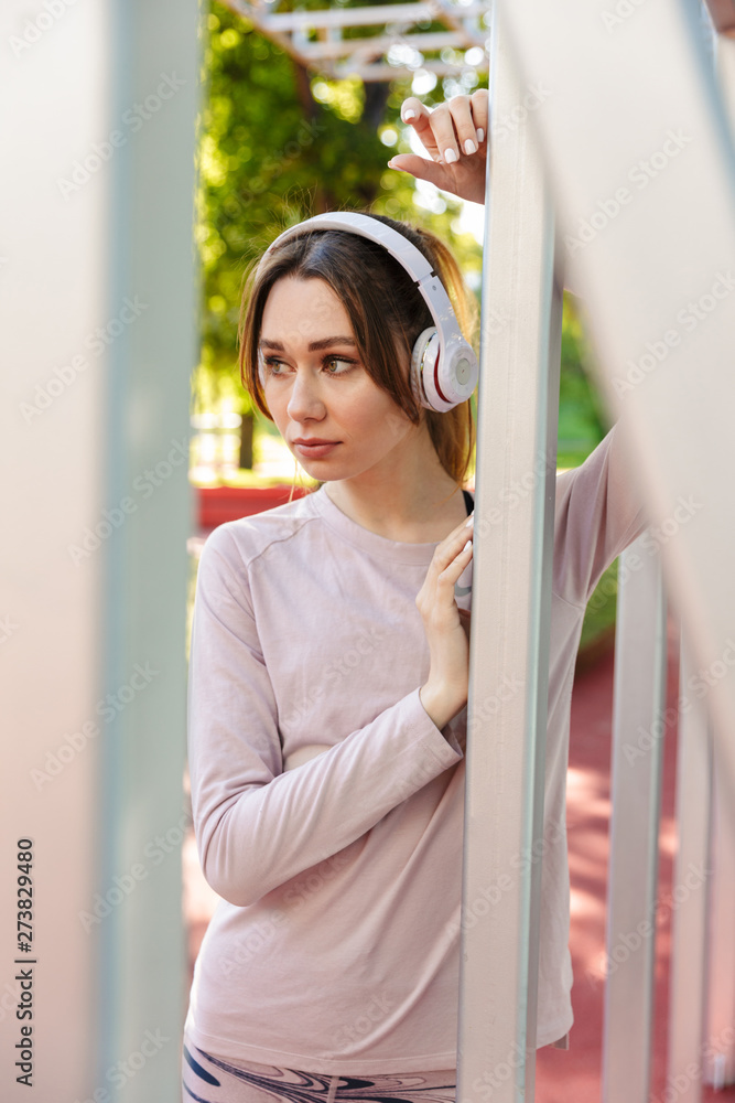Beautiful cheerful young fitness sports woman posing outdoors in park listening music with earphones.