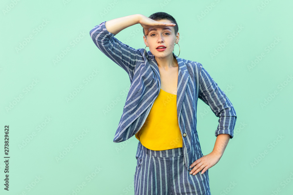 Portrait of attentive handsome beautiful short hair young stylish woman in casual striped suit standing with hand on forhead looking seriously. indoor studio shot isolated on light green background. Portrait of attentive handsome beautiful short hair young stylish woman in casual striped suit standing with hand on forhead looking seriously. indoor studio shot isolated on light green background.