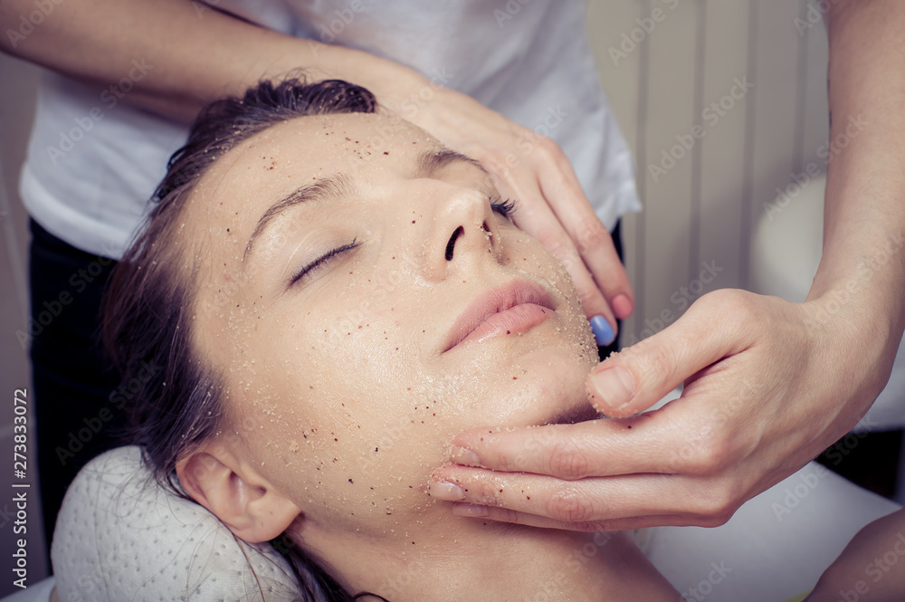 Cosmetician applying facial mask at young woman in spa salon