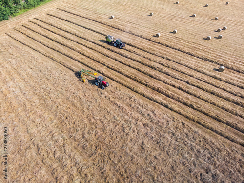 Nature and landscape, aerial view of fields with tractor with round baler and tractor with a rake, machines for collecting and pressing hay. Field with swaths ready to be transformed into round bales