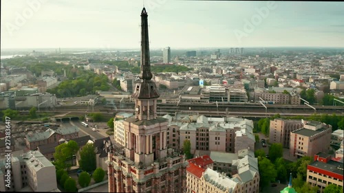 Aerial video of Riga city center, panning cityscape with a tower in front and bridges in the background, in a sunny afternoon. 4k footage.