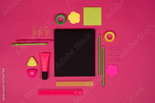 Black notebook with different school    colorful supplies on pink background. Back to school