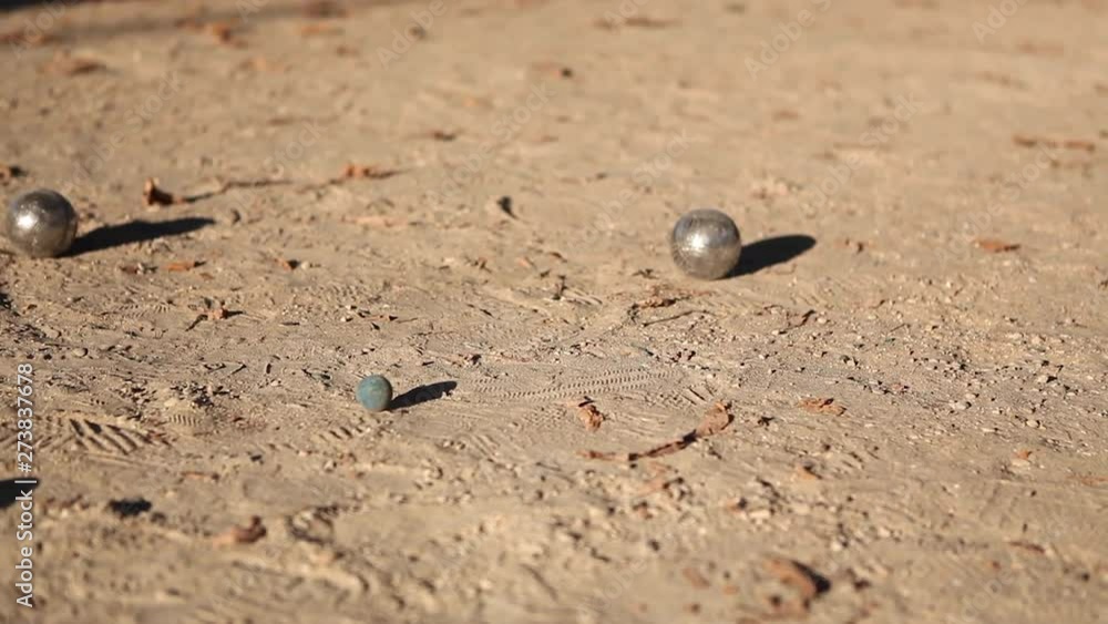 Clashes of metal balls during a game of petanque outdoors. Petanque player holding metal balls in his hand and shooting on a dirt floor in a sunny park in Paris in the summer afternoon. Metal impact. Clashes of metal balls during a game of petanque outdoors. Petanque player holding metal balls in his hand and shooting on a dirt floor in a sunny park in Paris in the summer afternoon. Metal impact.