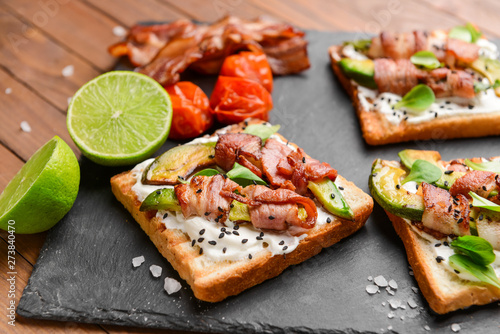 Tasty toasts with bacon on slate plate