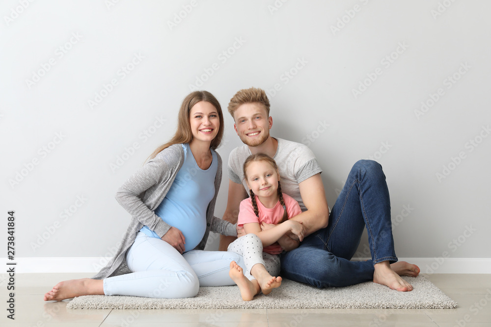 Beautiful pregnant woman with her family sitting near light wall Beautiful pregnant woman with her family sitting near light wall