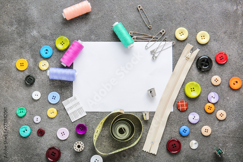 Set of sewing threads with accessories and sheet of paper on grey background