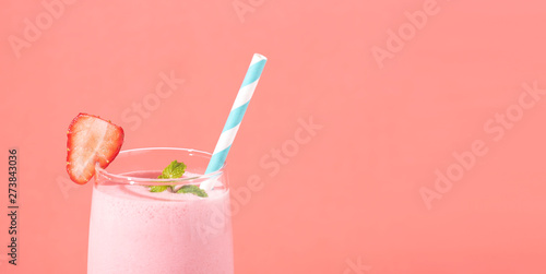 Fotografie, Obraz Strawberry smoothie in glass with straw and scattered berries on pink background
