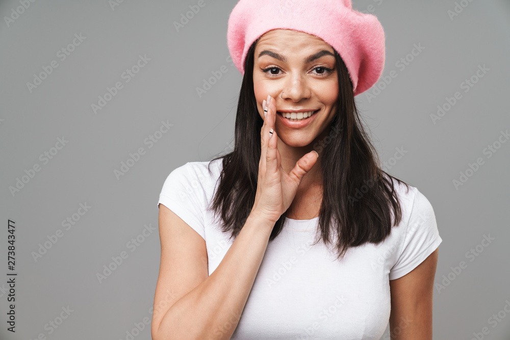 Photo closeup of young pretty woman in basic t-shirt and beret looking at camera and whispering while holding hand at her mouth Photo closeup of young pretty woman in basic t-shirt and beret looking at camera and whispering while holding hand at her mouth
