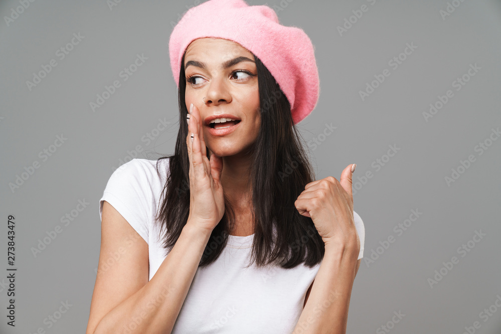 Photo closeup of cheerful pretty woman in basic t-shirt and beret looking at camera and whispering while holding hand at her mouth Photo closeup of cheerful pretty woman in basic t-shirt and beret looking at camera and whispering while holding hand at her mouth