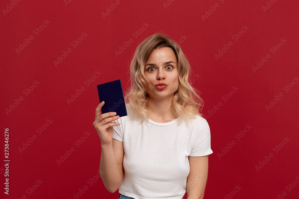 Portrait of a beautiful girl with curly blond hair dressed in a white t-shirt standing on a red background. Portrait of a beautiful girl with curly blond hair dressed in a white t-shirt standing on a red background.