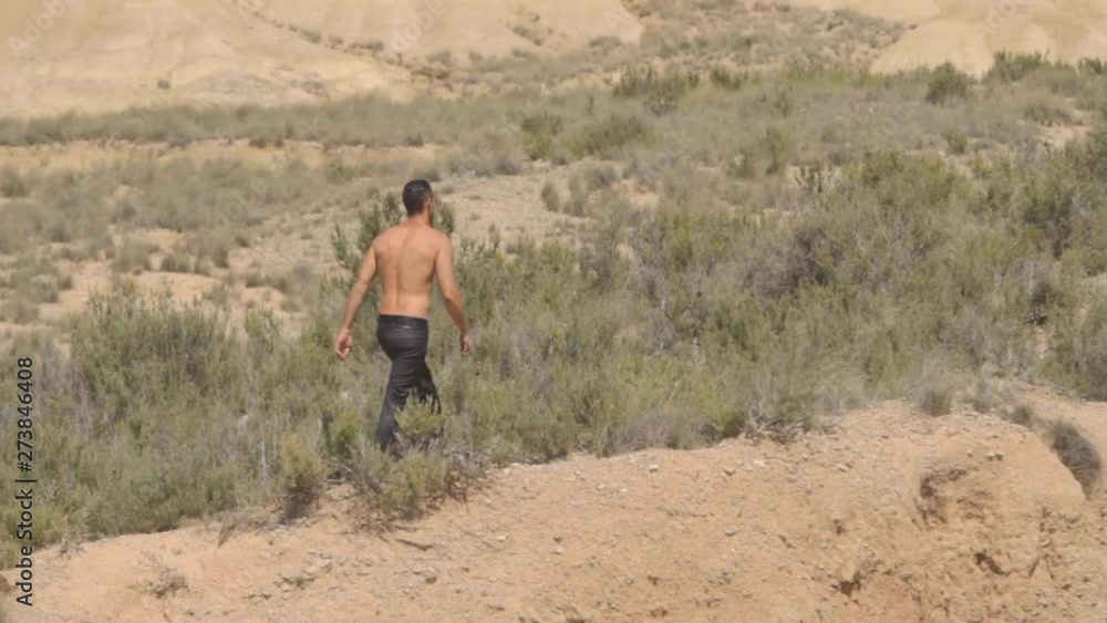 Handsome caucasian businessman, feeling freedom, with black suit pants, shirtless, walking in the desert to climb the mountain in sunny summer with a big sun. Spain.