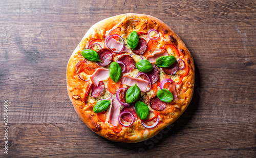 Pizza with Mozzarella cheese, ham, tomato sauce, salami, onion, pepper, Spices and Fresh basil. Italian pizza on wooden table background