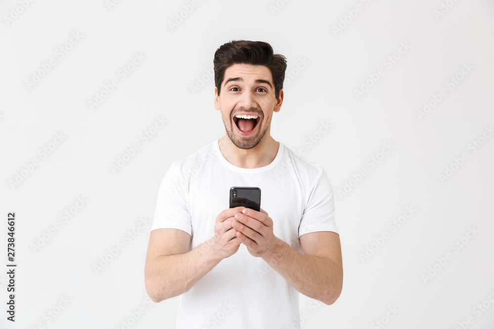Excited happy young man posing isolated over white wall background using mobile phone. Excited happy young man posing isolated over white wall background using mobile phone.