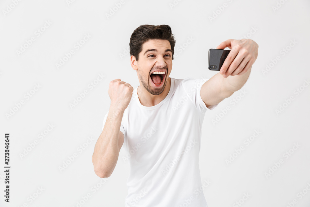 Happy emotional young man posing isolated over white wall background take selfie by mobile phone. Happy emotional young man posing isolated over white wall background take selfie by mobile phone.