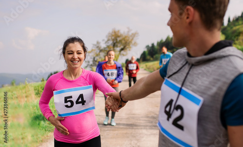 A man helping a pregnant woman in running competition in nature.