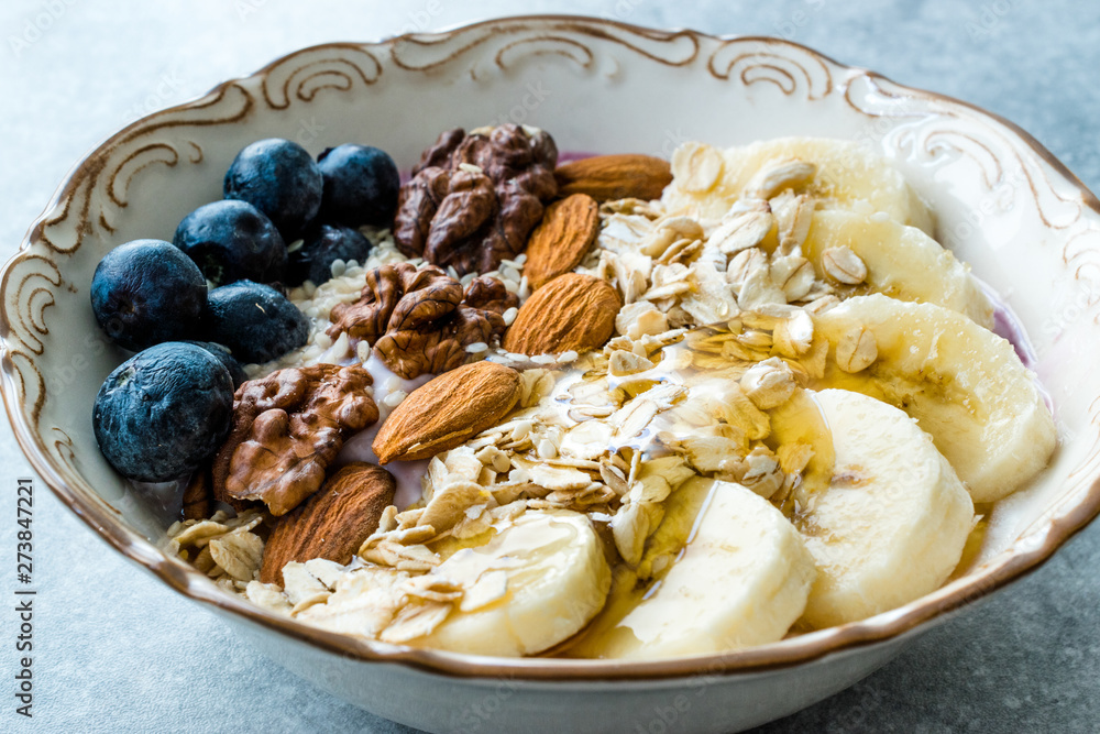 Acai Bowl with Yogurt, Blackberry, Banana Slices, Walnut, Honey, Jam, Oat, Almond, Sesame Seeds and Granola in Porcelain Bowl.
