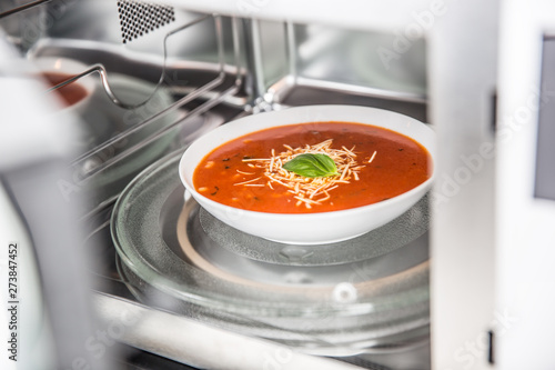 Inside view of new clean staniless microwave oven with a tomato soup in white plate photo