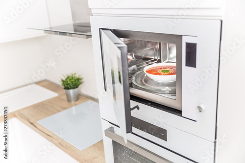 Built-in microwave oven  in the kitchen with tomato soup in white plate