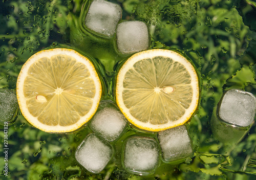 Slice of lemon and ice cubes on green background