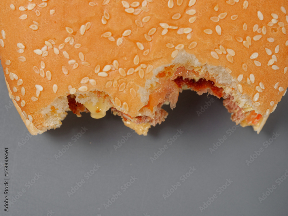 Obraz premium bitten big burger with cutlet cheese and tomato on a gray background