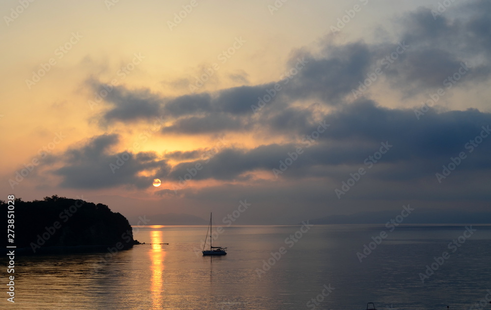 Seascape, lonely yacht. Setting sun in the clouds