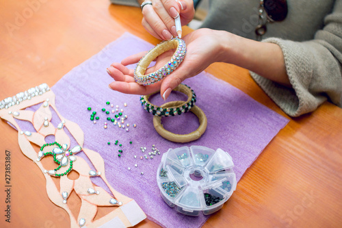 Photography Close-up woman`s hands, decorating bracelets with colorful shiny rhinestones, gluing crystals on a textile base with wax pencil
