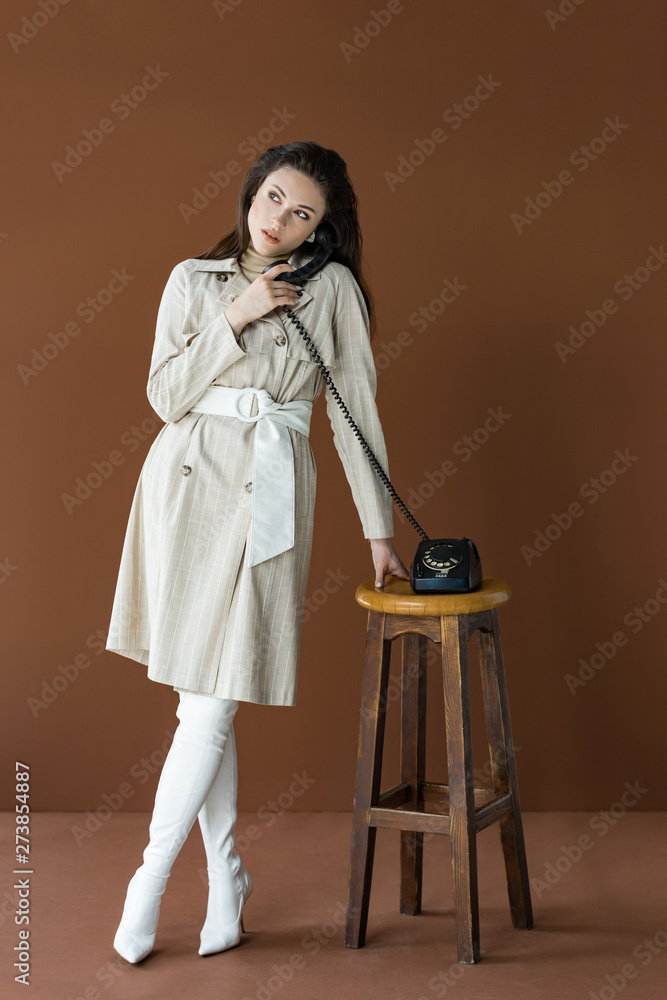 beautiful model in trench coat talking on telephone, looking away and standing isolated on brown beautiful model in trench coat talking on telephone, looking away and standing isolated on brown