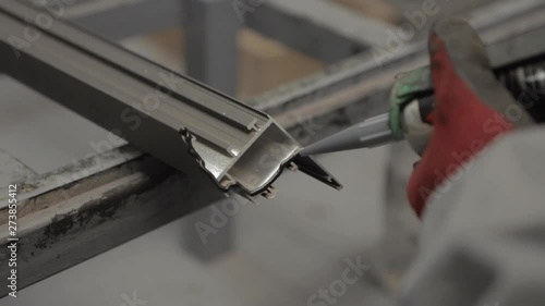 Worker applying black silicone sealing with caulking gun for moisture protection on window, processing of aluminum parts in a Production of aluminium Windows Workshop. Manufacturing of windows.