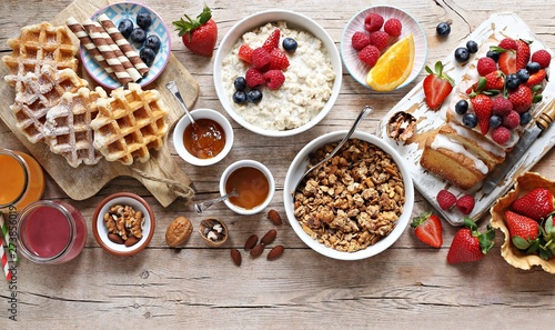 Happy breakfast with granola, oatmeal porridge, smoothies, fresh waffles, sweets, fruits and berries.
