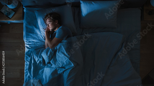 Top View of Handsome Young Man Sleeping Cozily on a Bed in His Bedroom at Night. Blue Nightly Colors with Cold Weak Lamppost Light Shining Through the Window. photo