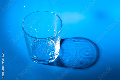 A glass with water drops on a dark blue background close up