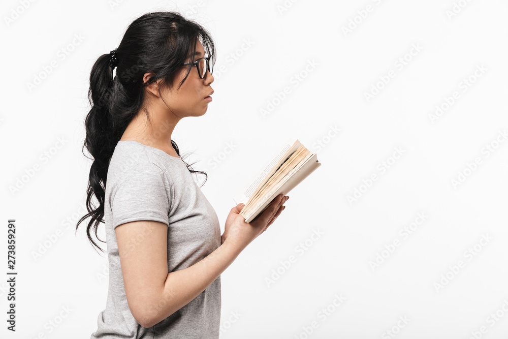 Beautiful young woman posing isolated over white wall background holding book reading.