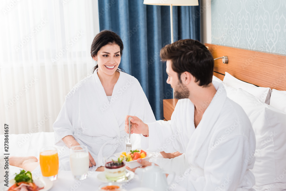 selective focus of happy woman looking at bearded man holding fork near fruit salad