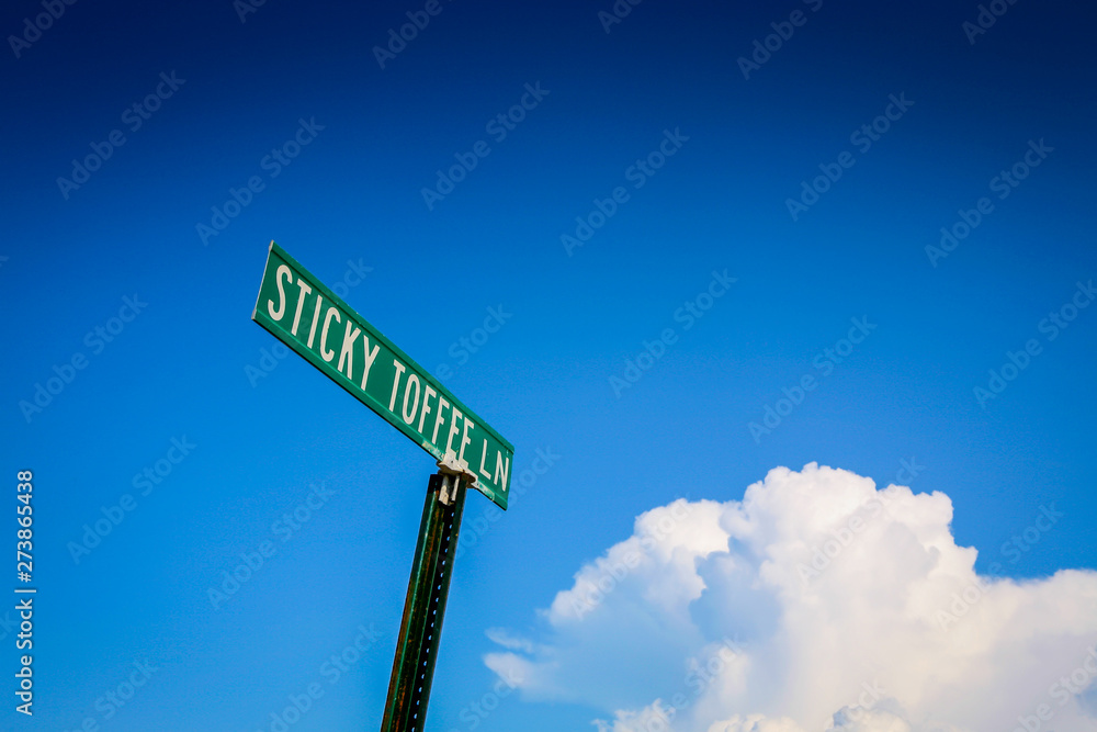 Fototapeta premium street sign for sticky toffee land with blue sky and fluffy cloud
